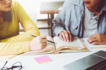 Two people studying with books and a laptop on a table.