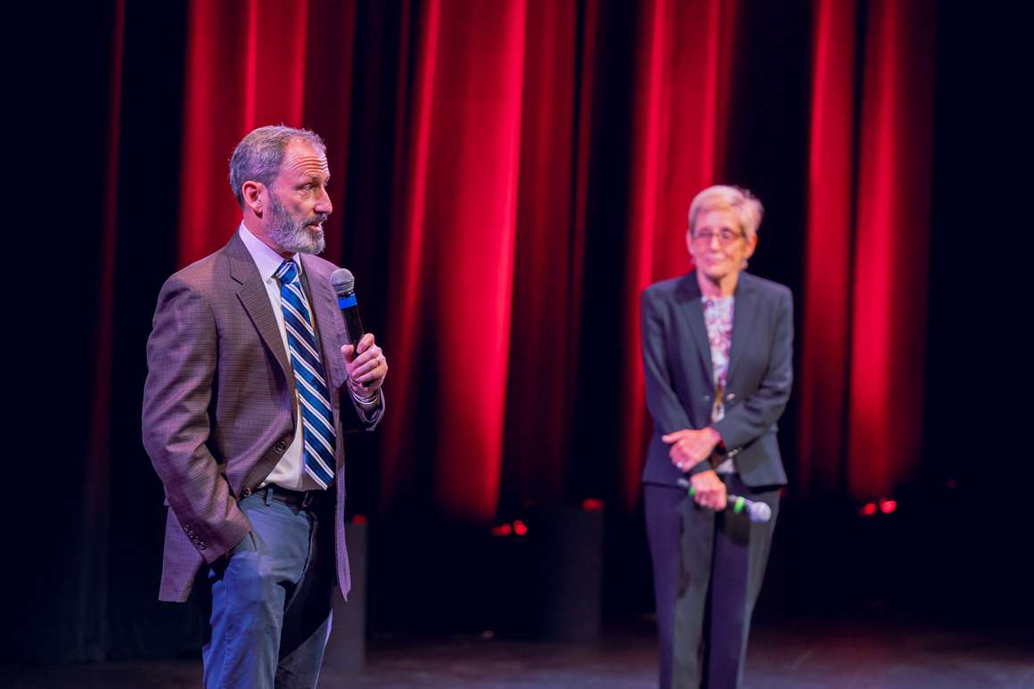 Provost Glaser speaking on stage with President Sullivan standing behind him