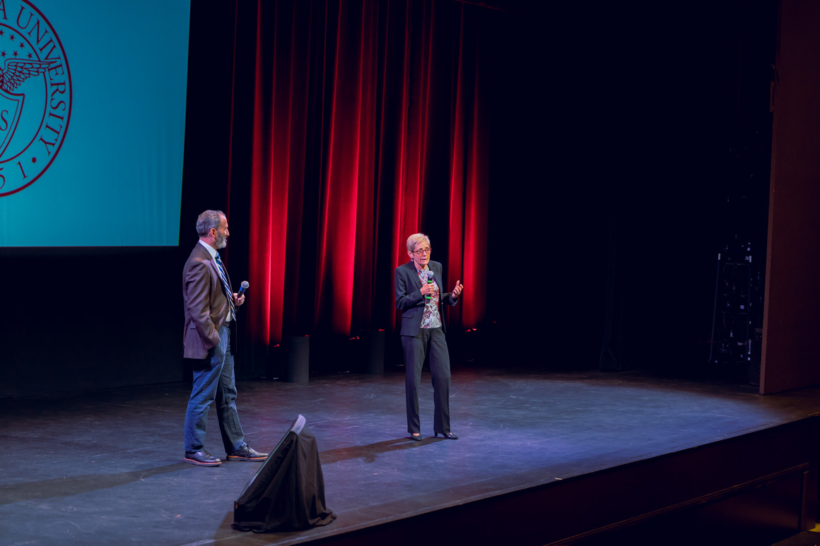 President Sullivan speaking on stage with a Provost Glaser