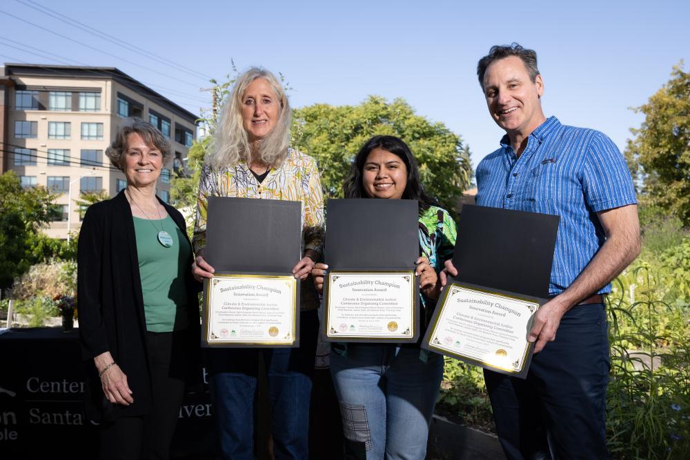 Three people smiling with their Sustainability Champion Award certificates next to an event coordinator