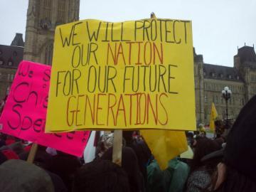 Alt text: Protesters hold a yellow sign reading 