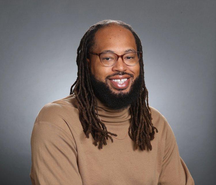 A Black person in a brown turtleneck and glasses.