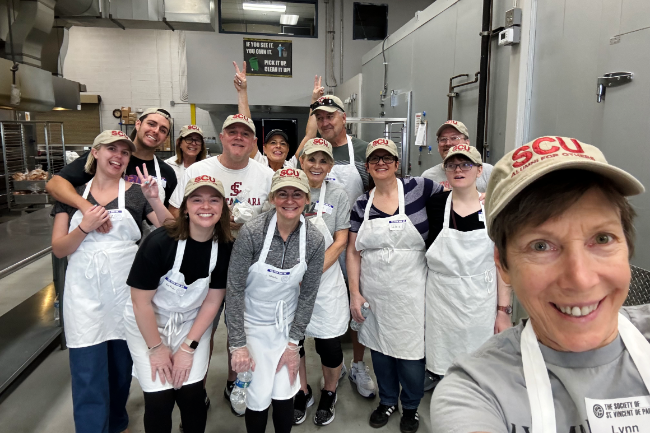 SCU Alumni in a kitchen with aprons and SCU merch baseball caps