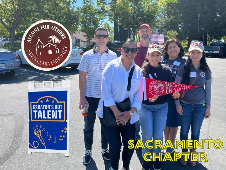 Group of people holding a Santa Clara University pennant. A cutout of a sign reading 