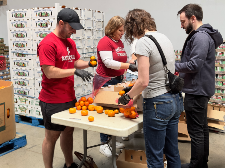Several people in Santa Clara University shirts packing fruit into boxes on a table.