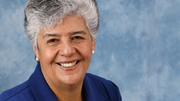 A smiling woman with short, grey hair in front of a light blue background.