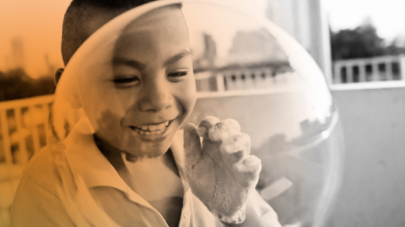 A child laughing behind a large soap bubble