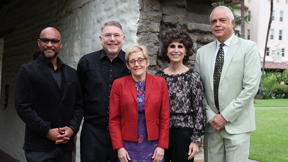 Three men and two women smiling in formal outfits.