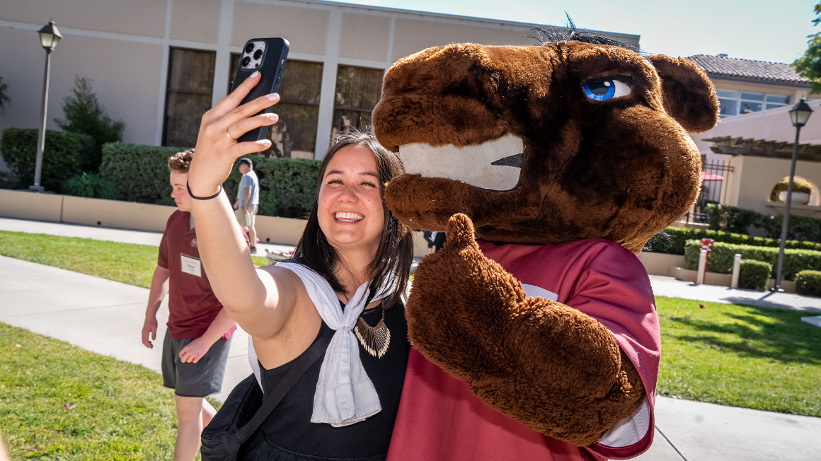 Young alumna taking a selfie with Bucky Bronco 