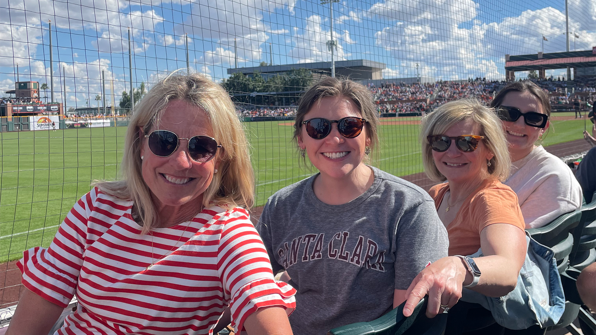 Four alumnae sitting with their backs to a baseball field