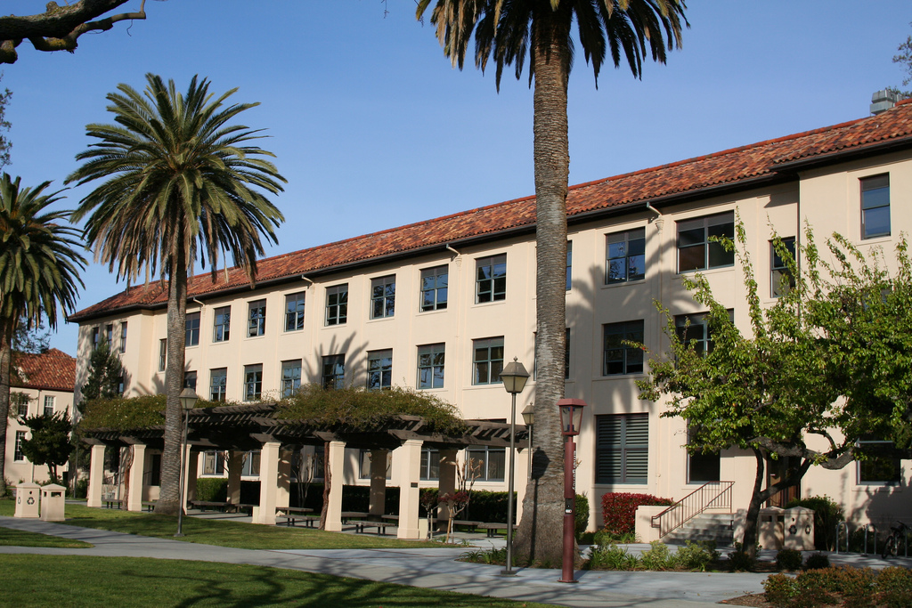 Kenna Hall, a three-story beige building with palm trees and a garden. 