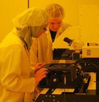Two individuals in lab coats working with scientific equipment under yellow lighting.