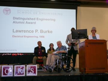 Photo of Distinguished Engineering Alumni Award winner, Lawrence Burke, on a stage accepting the award Dean Elaine Scott is announcing at a podium.