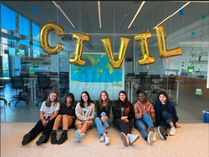 Seven female students sitting on the floor in front of the Geotech Lab with big balloons spelling out 