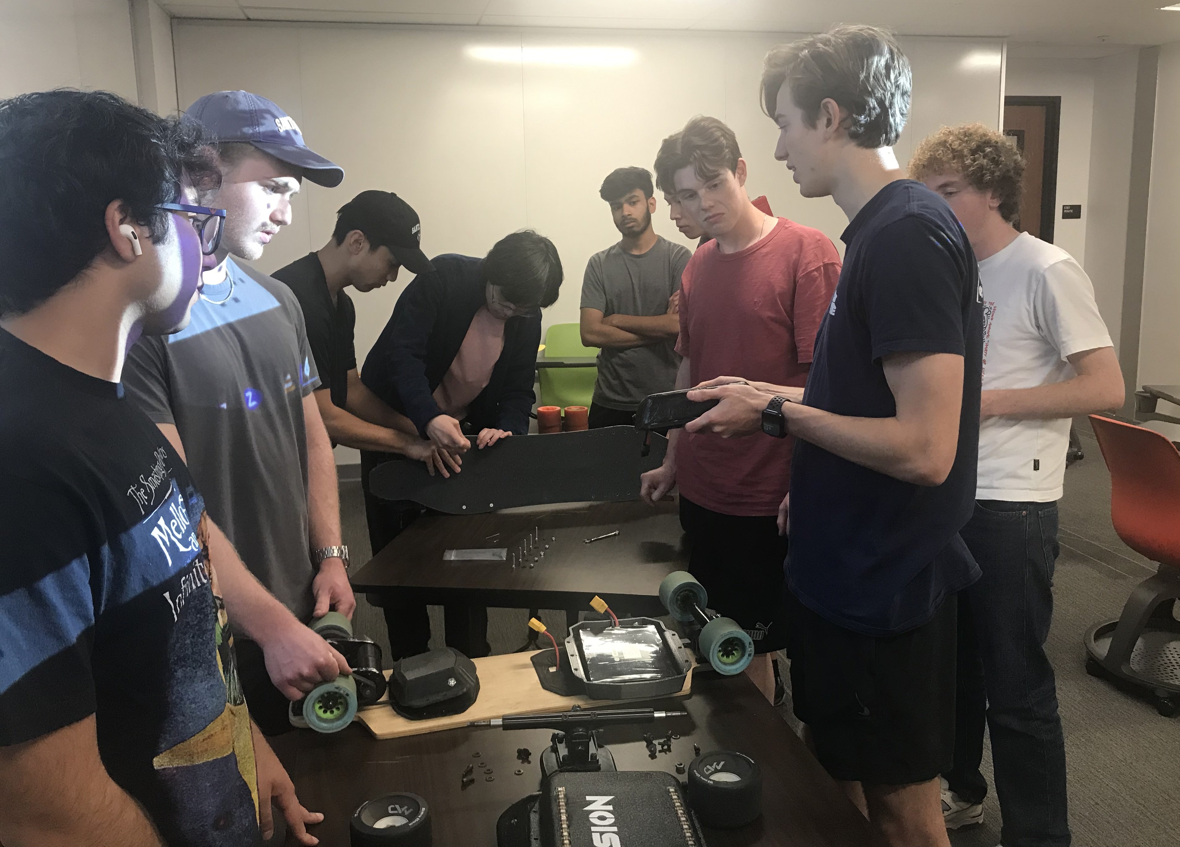 Nine male ASME members tearing down an E-Skateboard